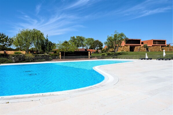 A swimming pool with a curved edge, surrounded by a paved area and a fence. - L'Orangerie (Vilamoura)