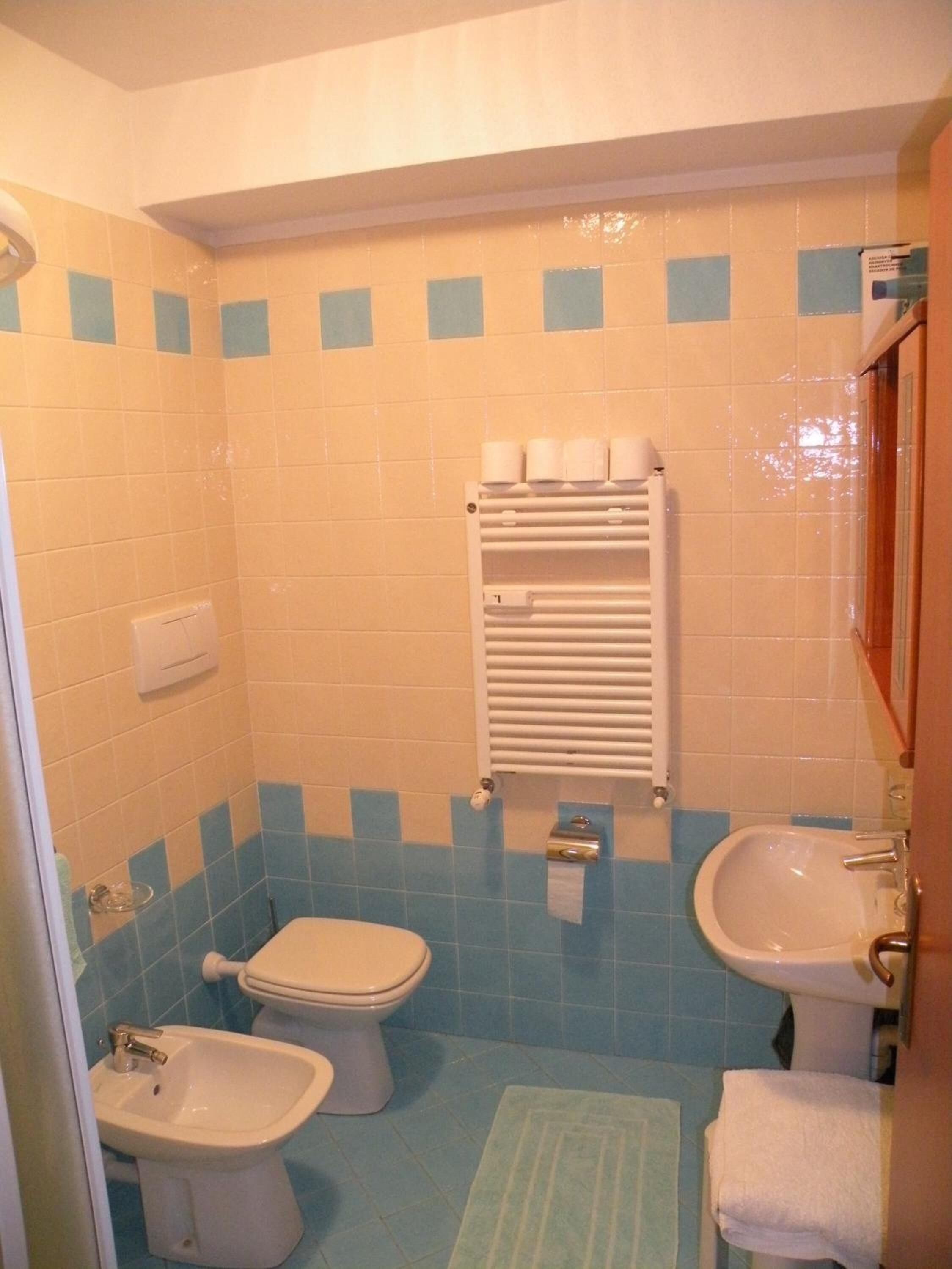 A bathroom with a toilet, bidet, sink, and towel rack.
