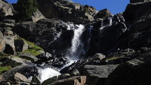 Una cascada desciende sobre terreno rocoso bajo un cielo azul despejado.