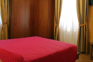 Ein Zimmer mit Bett, Holzschrank und Vorhängen.