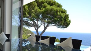 A glass table with four chairs, each with a white pillow, overlooking a tree and the ocean. - Large, Luxury Villa, Sea Views, Heated Pool in Begur, Costa Brava (La Borna)