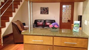 A kitchen with wooden cabinets, a granite countertop, a vase with flowers, a black leather couch, and a staircase. - Casa Nuno e Lorena - Ideal location and privacy. (Sao Roque)