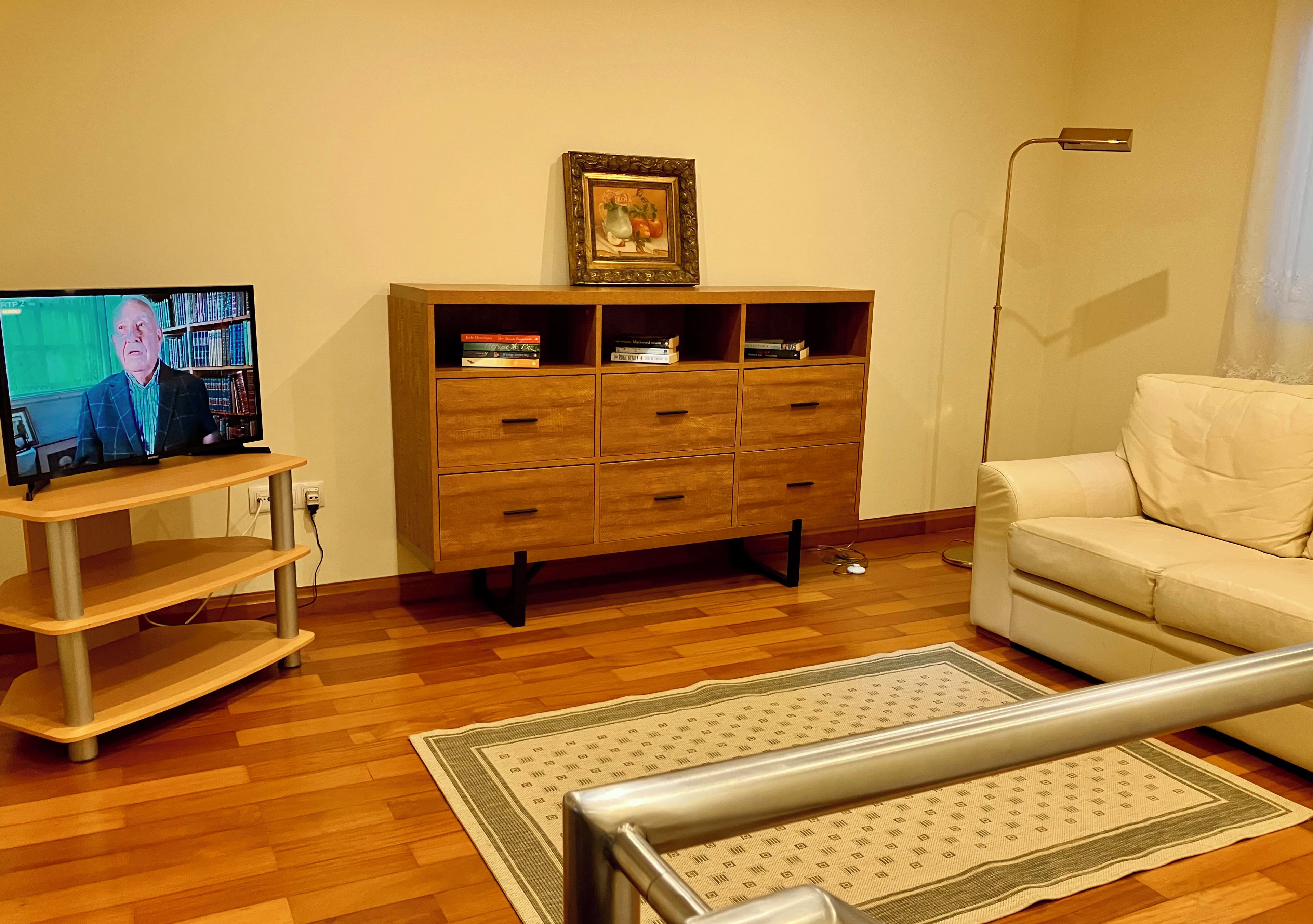 Un salon avec un meuble en bois, un téléviseur, un canapé blanc et un tapis à motifs.