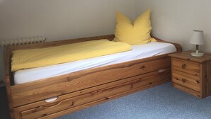 A wooden bed with a yellow blanket and pillows, a bedside table with a lamp, and a radiator on the wall. - Vacation apartment for 2 -3 persons in the beautiful Weserbergland (Hessisch Oldendorf)