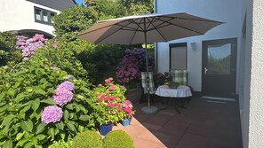 Un espace patio aménagé avec une table et des chaises, entouré de plantes et de fleurs en pot.