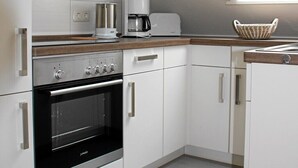 A modern kitchen with white cabinets, a black oven, a coffee maker, and a skylight. - Vacation apartment for 2 -3 persons in the beautiful Weserbergland (Hessisch Oldendorf)