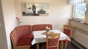 A dining area with a booth seating arrangement, a table with a white tablecloth, and a window with a view of trees. - Vacation apartment for 2 -3 persons in the beautiful Weserbergland (Hessisch Oldendorf)