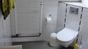 A modern bathroom with a skylight, white tiles, a toilet, and a towel rack with green towels. - Vacation apartment for 2 -3 persons in the beautiful Weserbergland (Hessisch Oldendorf)