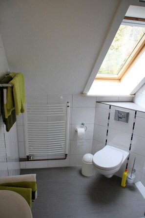 Ein modernes Badezimmer mit Dachfenster, weißen Fliesen, einer Toilette und einem Handtuchhalter mit grünen Handtüchern.