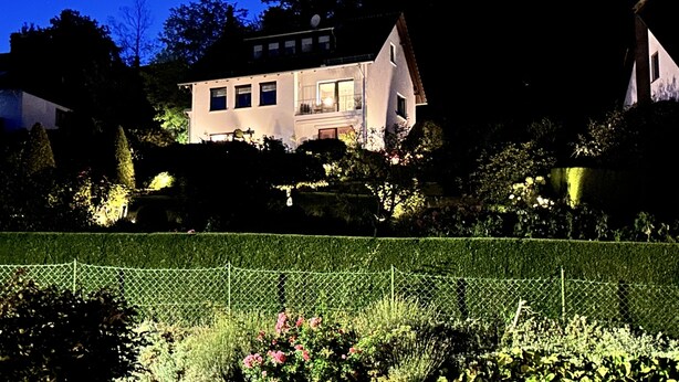 Ein großes Haus mit einem gepflegten Garten und einer Hecke im Vordergrund.