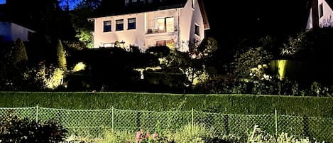 Ett stort hus med en välskött trädgård och en häck i förgrunden.