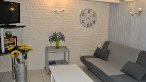 A living room with a stone wall, a clock, a television, a sofa, a coffee table, and a vase with flowers. - Quiet 40m² cottage with private courtyard (La Tour-Saint-Gelin)
