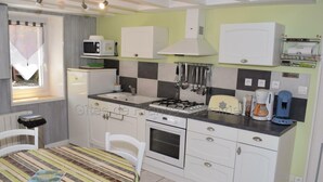 A compact kitchen with a gas stove, microwave, and a small refrigerator. There is a dining table with chairs and a striped tablecloth. - Quiet 40m² cottage with private courtyard (La Tour-Saint-Gelin)