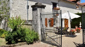 A stone building with a tiled roof, a gated entrance, outdoor seating, and potted plants. - Quiet 40m² cottage with private courtyard (La Tour-Saint-Gelin)