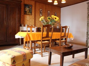 A dining area with wooden walls, a yellow tablecloth-covered table, and chairs. Sunflowers are in a vase on the table. - Quiet 3-room house near the beach in La Brée-les-Bains (La Brée-les-Bains)