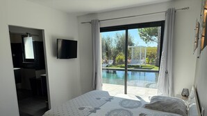 A bedroom with a large bed, a TV, and a view of a swimming pool and garden. - Contemporary wine estate villa with infinity pool (Servian)