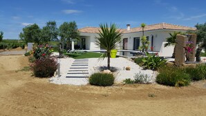 A modern house with a tiled roof, surrounded by a well-maintained garden with various plants and a gravel pathway leading to the entrance. - Contemporary wine estate villa with infinity pool (Servian)