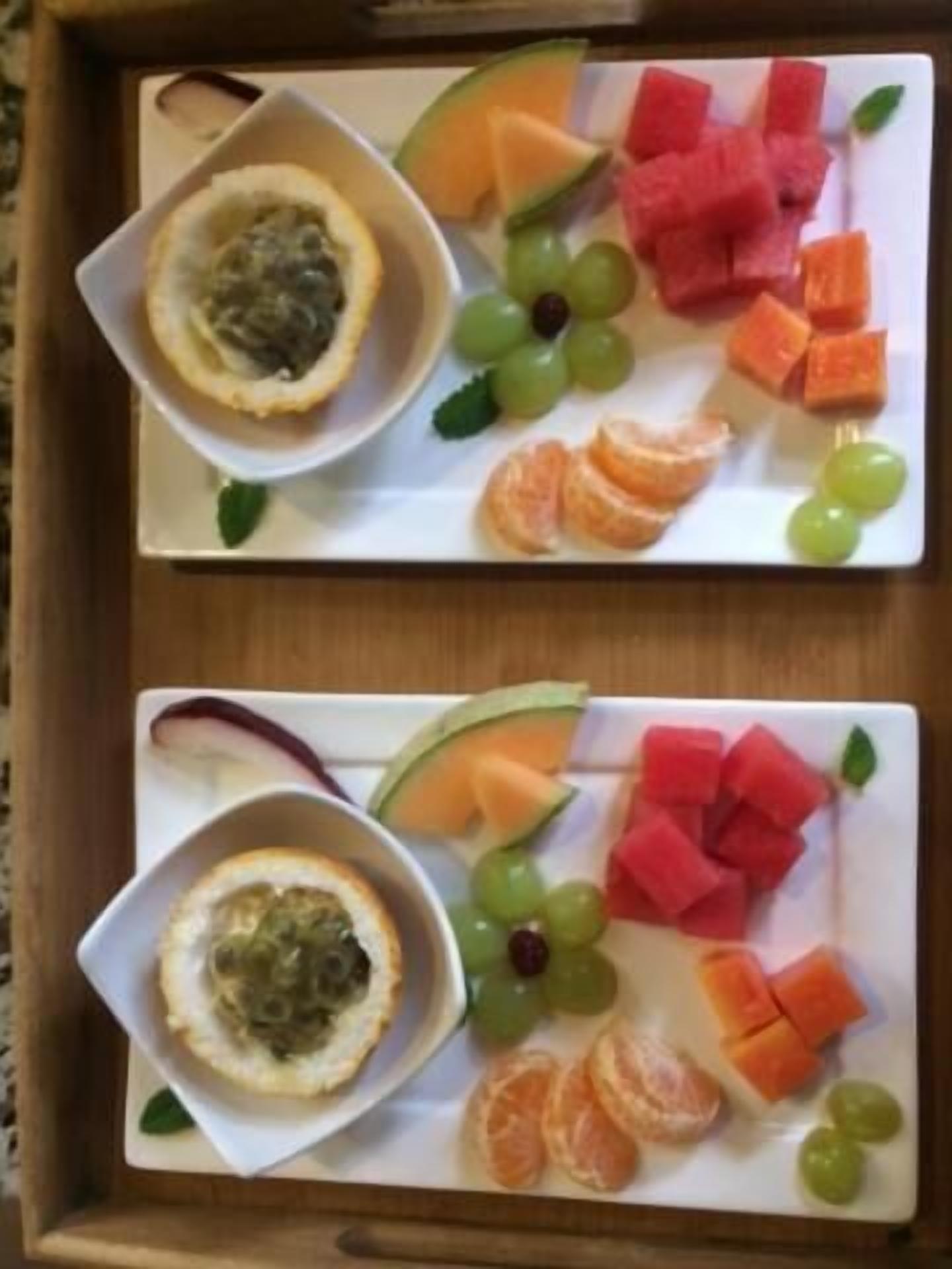 Een dienblad met twee borden eten, elk met verschillende soorten fruit en een klein bakje dip.