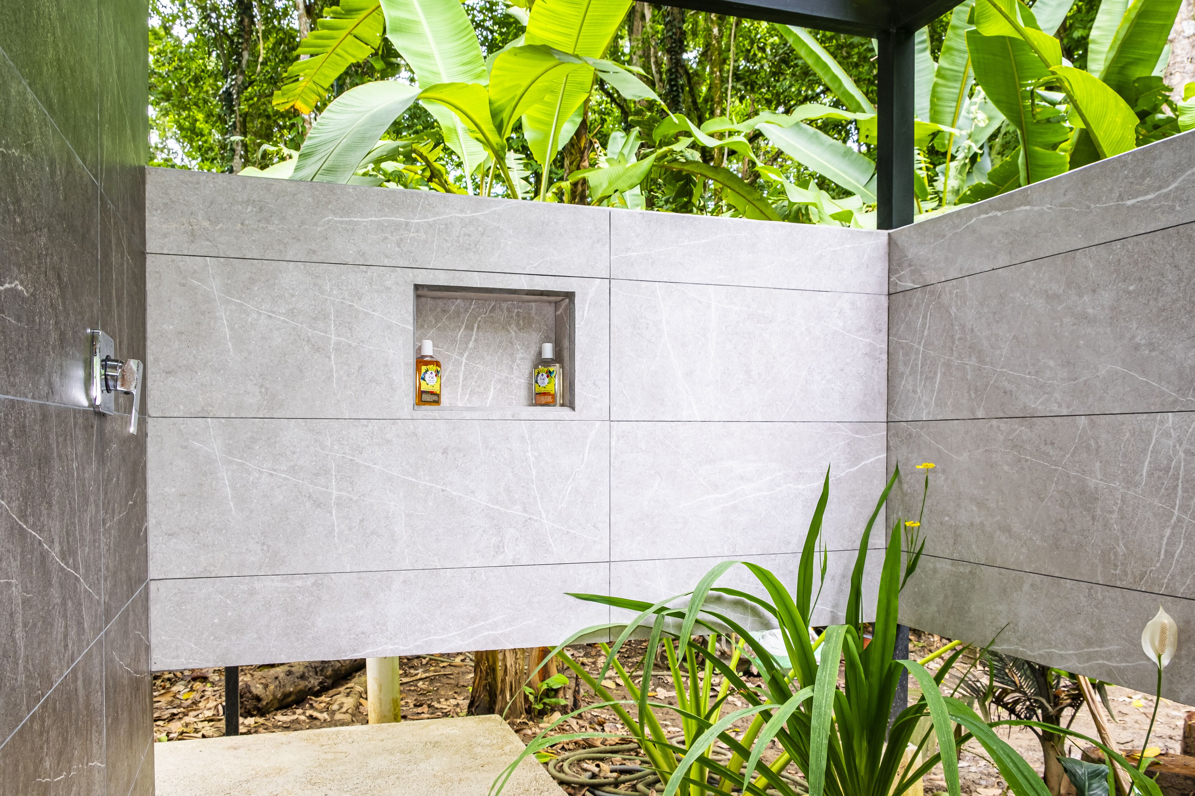 A modern bathroom with a built-in shower and two bottles of shampoo in a shelf.