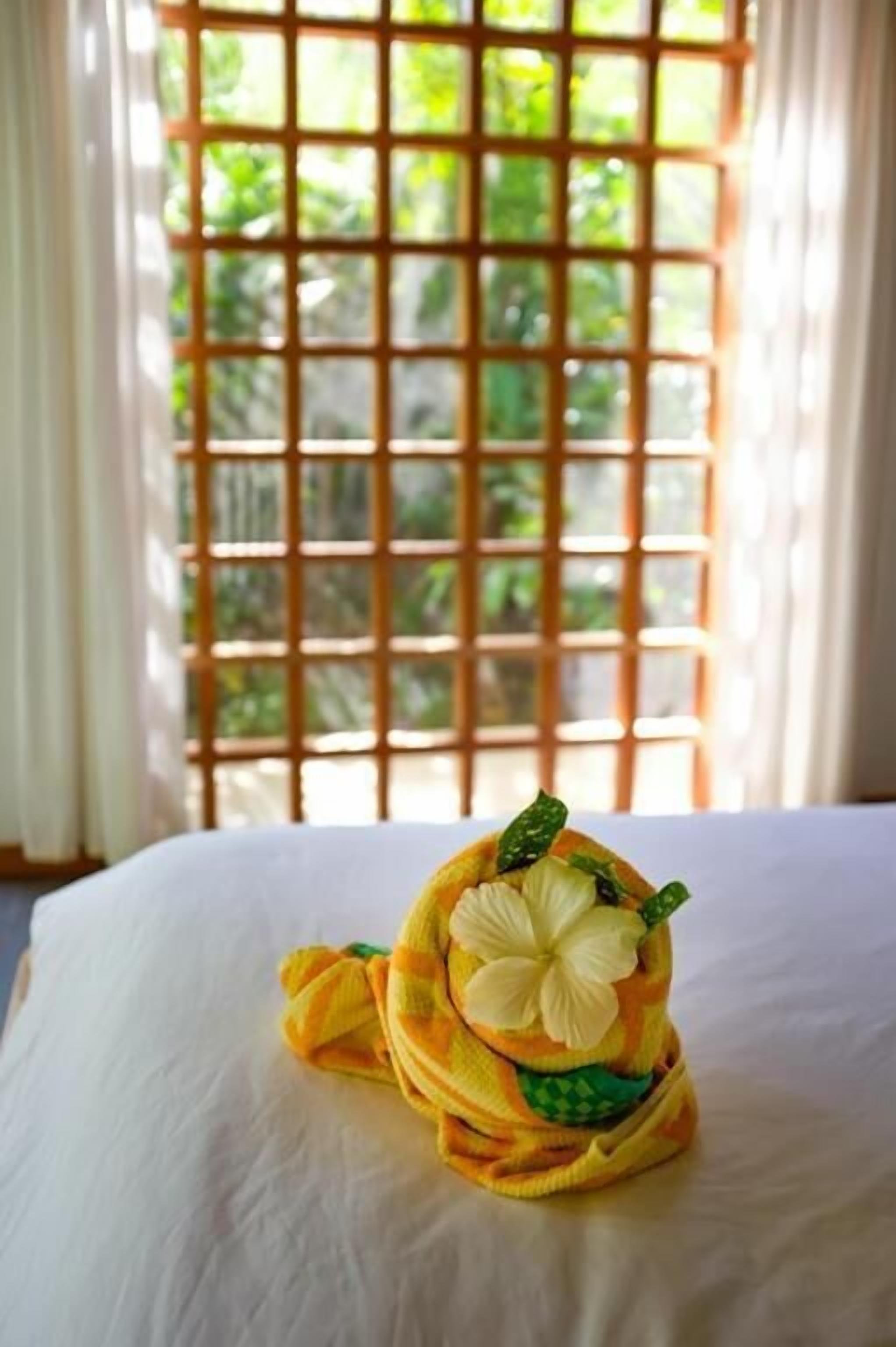 A neatly made bed with a decorative pillow featuring a white flower and green leaves.