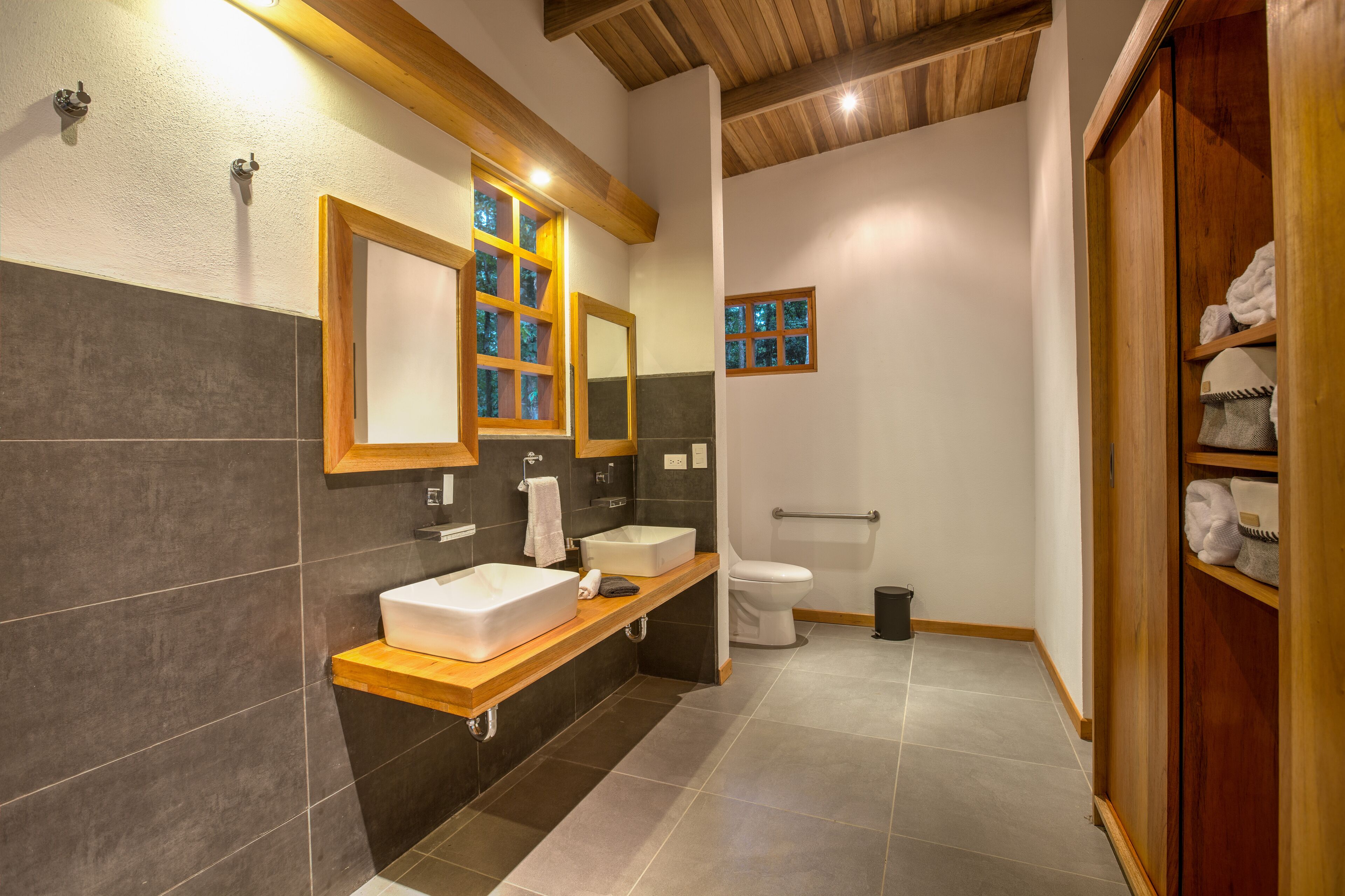 Ein modernes Badezimmer mit einem Holzwaschtisch, einem großen Spiegel, einer Toilette und einem Duschbereich.