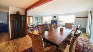 Un vaste espace dédié à la salle à manger, avec une table en bois et des chaises en osier, une cheminée et de grandes fenêtres offrant une vue sur l’extérieur.