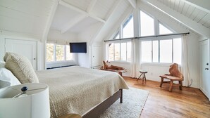 Une chambre avec un grand lit, un téléviseur fixé au mur et une chaise en bois.