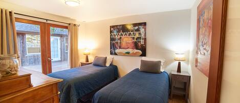 A bedroom with two beds, a wooden dresser, a painting on the wall, and a window with curtains.