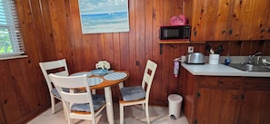 Interior de madeira com uma mesa de jantar, cadeiras, micro-ondas, pia e uma pequena lixeira.