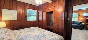 Een slaapkamer met houten lambrisering, een bed met bloemenbedrukking, een raam met uitzicht en een inbouwkast.