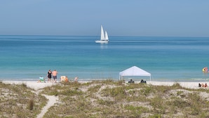 A beach with a sailboat, a tent, and people relaxing. - Beachfront Cottages PATIO at Beautiful Sandy Shores on the Gulf of America (INDIAN ROCKS BEACH)