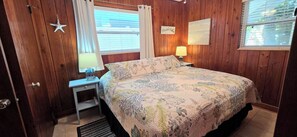 Une chambre à coucher avec un lit, une table de chevet, une lampe, une décoration en forme d’étoile de mer et une fenêtre avec des stores.