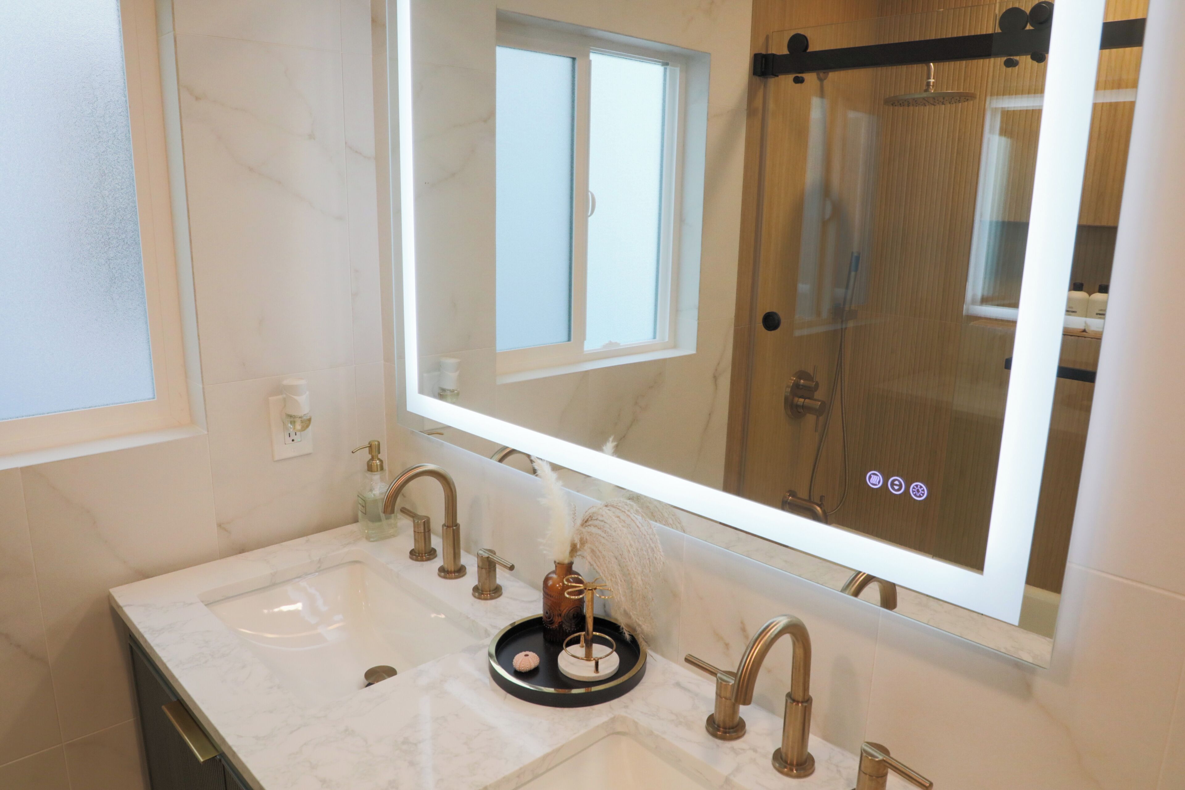 Un baño con un espejo grande, un lavabo con encimera de mármol y una zona de ducha.