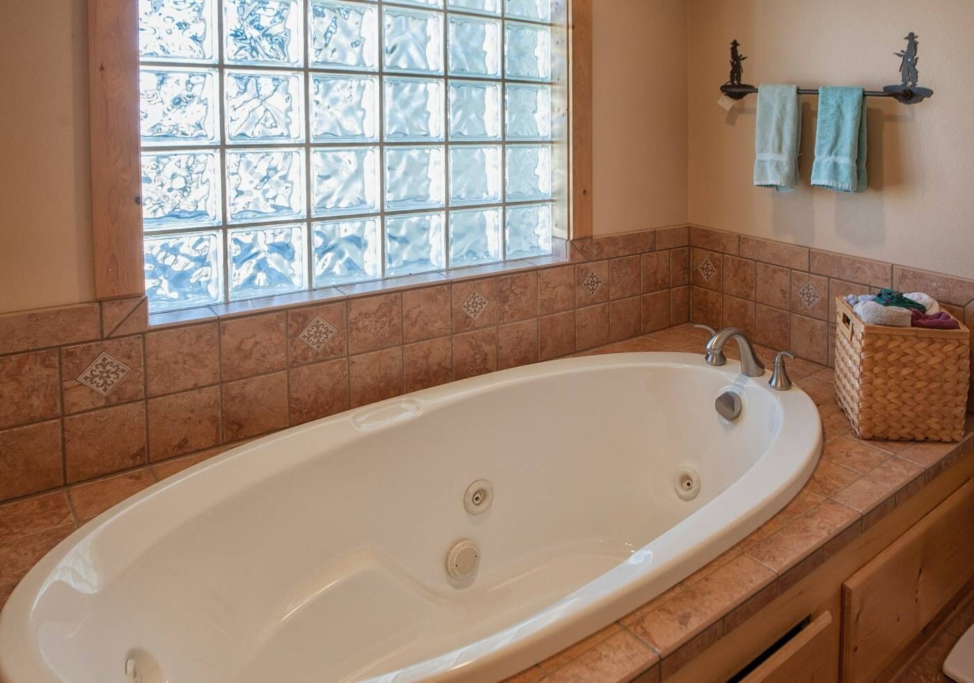 A bathroom with a large bathtub, a window with frosted glass, and a towel rack with two towels.