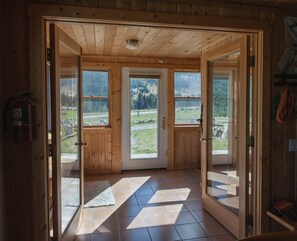 A wooden cabin with three glass doors leading to a tiled floor and a view of a mountainous landscape. - Mountain Views From Every Direction (Red Lodge)