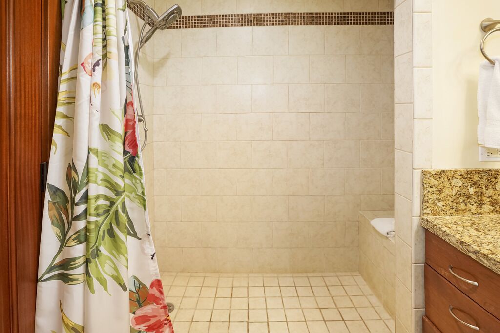 A bathroom with a shower, tiled walls, and a wooden cabinet with drawers.