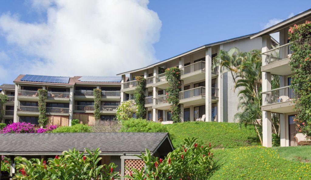 Un hôtel à plusieurs étages doté de balcons, de panneaux solaires et d’un aménagement paysager luxuriant.