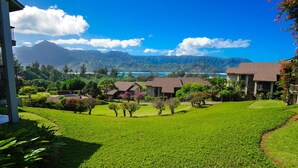 A residential area with houses, a well-maintained lawn, and a mountain range in the background. - Aloha Condos, Hanalei Bay Resort, Condo 6304, Ocean View, AC (Princeville)