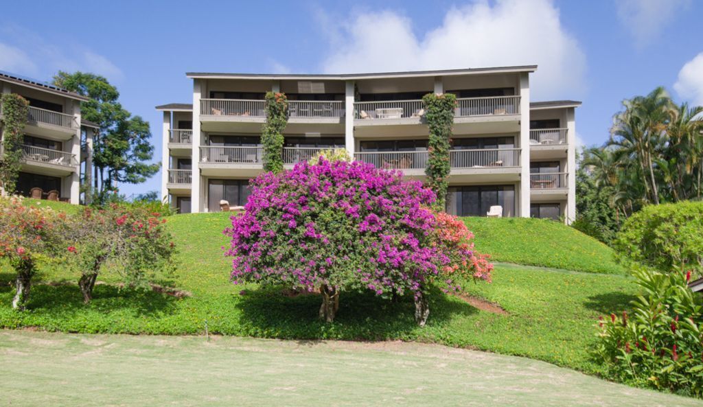 Un hotel a più piani con un giardino rigoglioso e un cespuglio fiorito di colore viola in primo piano.