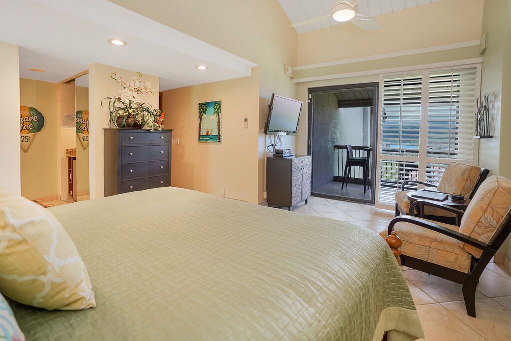 A bedroom with a large bed, a dresser, a TV, and a balcony with a chair.
