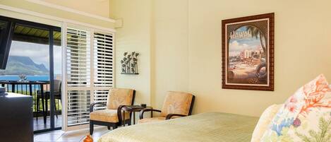 A hotel room with a bed, two chairs, a table, and a balcony with a view of the ocean.