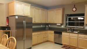 A kitchen with wooden cabinets, a stainless steel refrigerator, a dishwasher, and a window with a view of the outside.