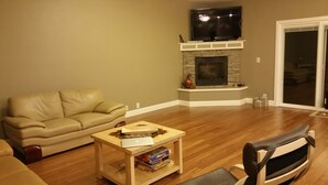 A living room with a stone fireplace, a ceiling fan, and a shelf with books.