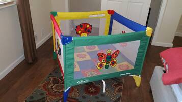 Un parc pour enfants aux couleurs vives, orné de motifs de papillons, posé sur un tapis à motifs dans une pièce au plancher en bois, avec une porte visible au fond.