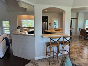 A modern kitchen with a central island, bar stools, and a dining area with wicker chairs.
