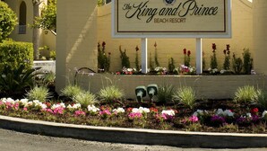 A resort sign with a palm tree and flowers in front. - King & Prince Oceanfront North Villa (St Simons Island)