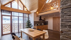 A spacious dining area with a wooden table and chairs, a kitchen in the background, and a view of mountains through large windows.