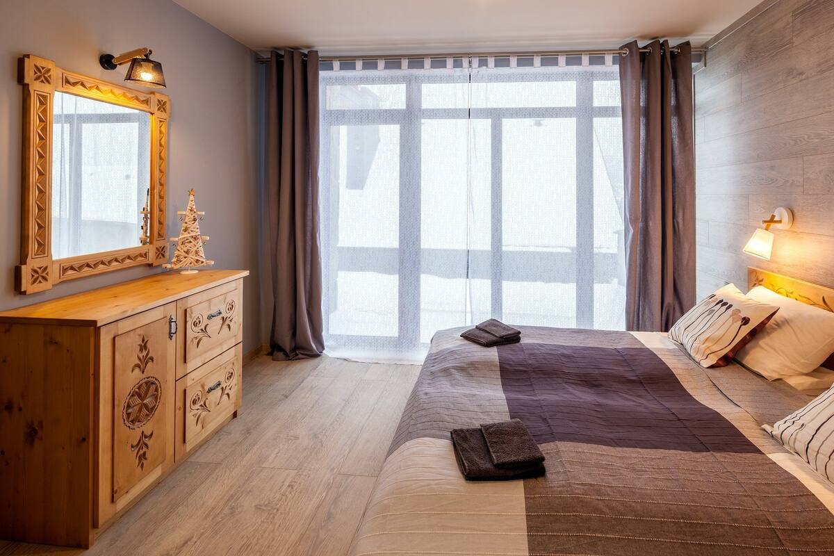 A bedroom with a large bed, wooden dresser, and a mirror.