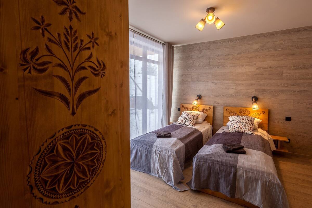 A hotel room with two beds, wooden headboards, and a large window with sheer curtains.