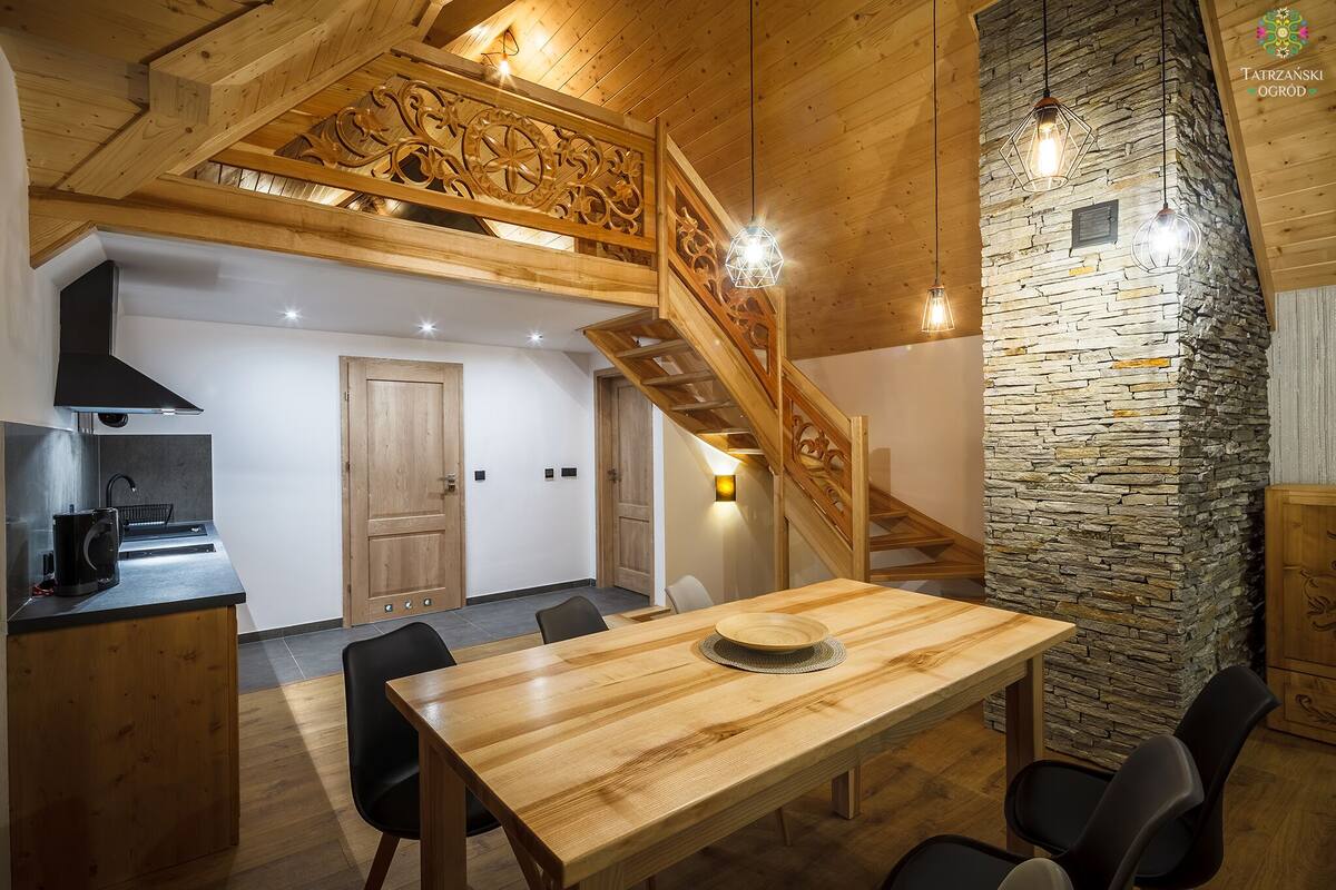 A modern kitchen with a wooden island, a stone accent wall, and a wooden staircase.